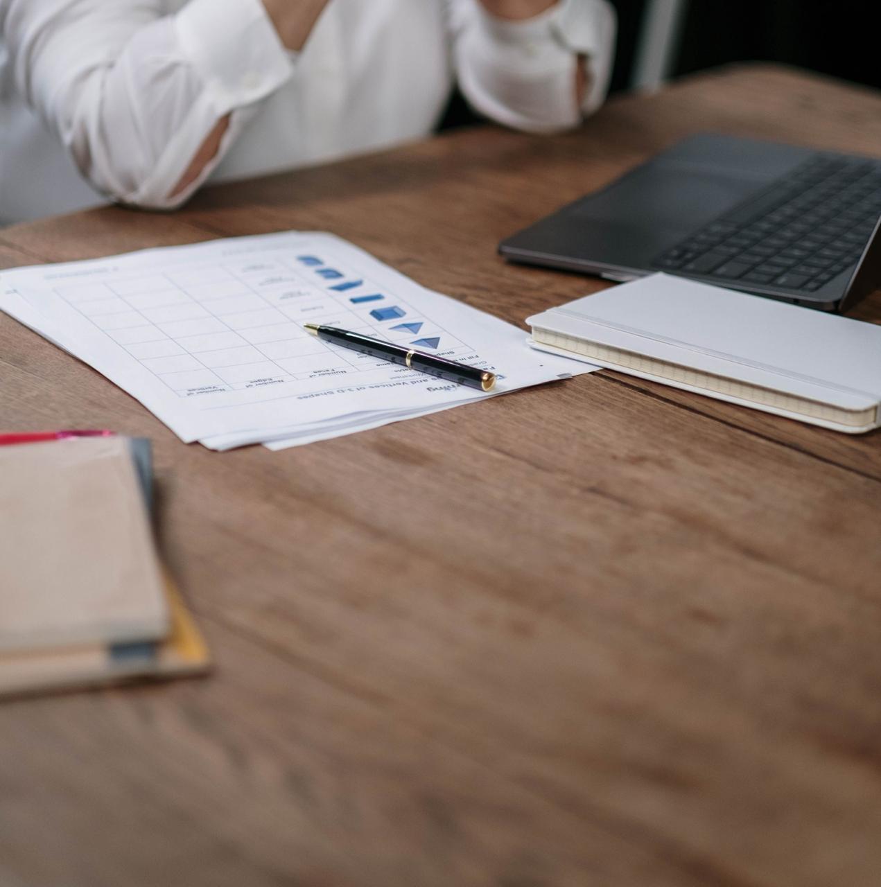 Mesa de trabalho com laptop, relatórios impressos, caderno e caneta durante a operação financeira