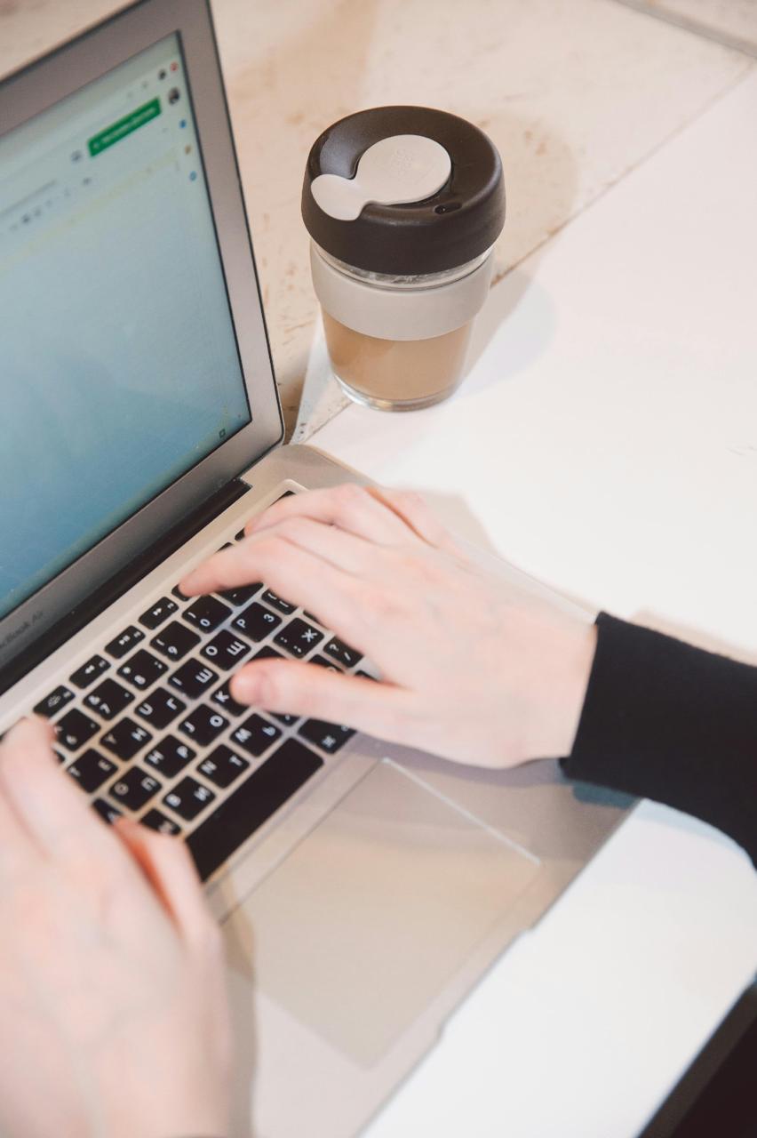 Empresária trabalhando no laptop com uma xícara de café ao lado, executando a rotina financeira
